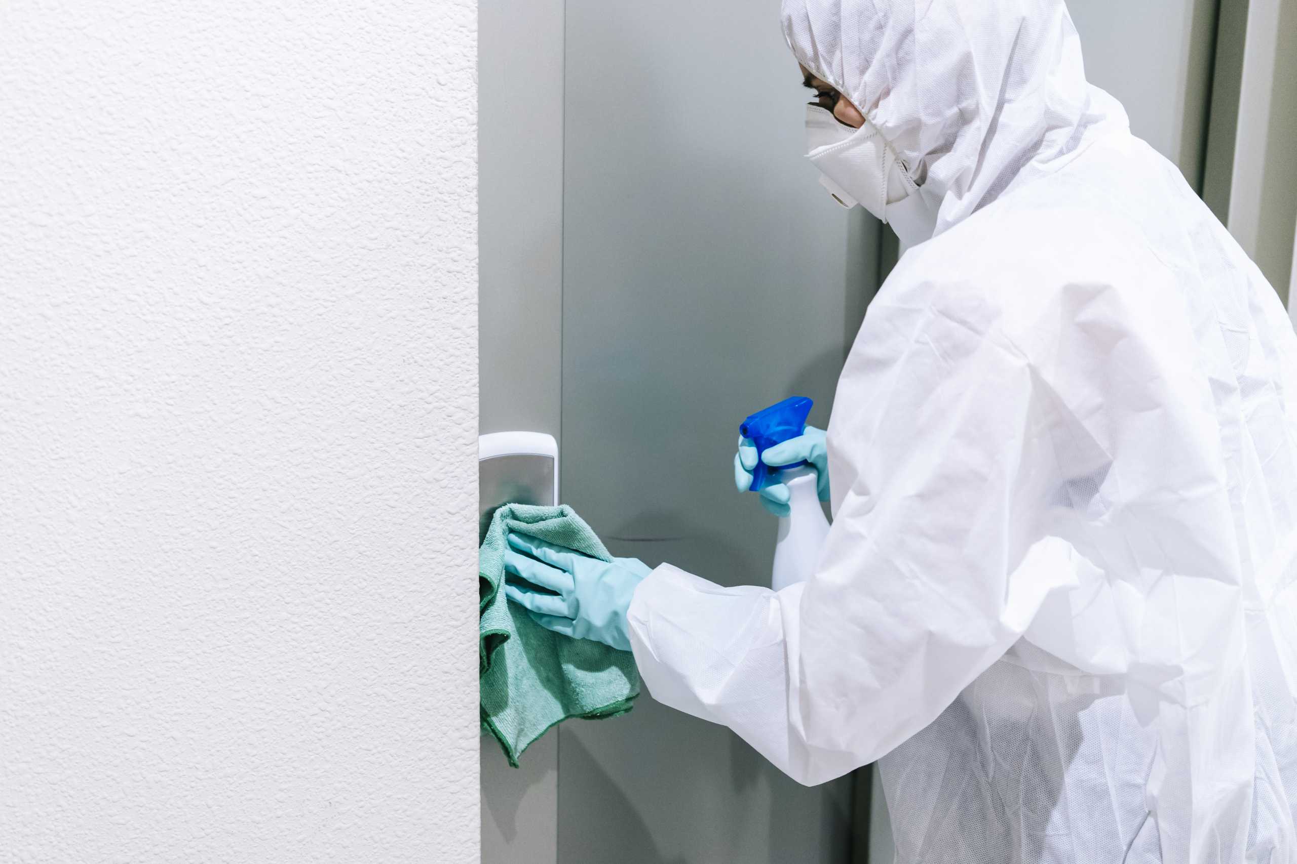 A person protected with safety clothing against a pandemic or virus, cleans and disinfects a portal of a house